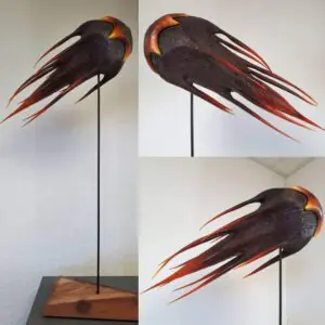 A full-view, professional photograph of the "Comet of Kaos," a colorful wooden sculpture with a star-shaped head and long, flowing tails. The sculpture is made from laminated maple and mounted on a steel rod and a sandblasted Sequoia base.