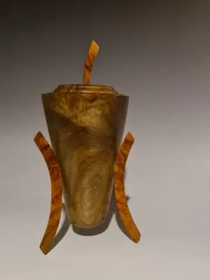 Professional photo of the "Rocket Pot" sculpture, a wooden vessel with a lid and three legs. The body is dark black walnut and the legs are a light, figured New Zealand Rimu.