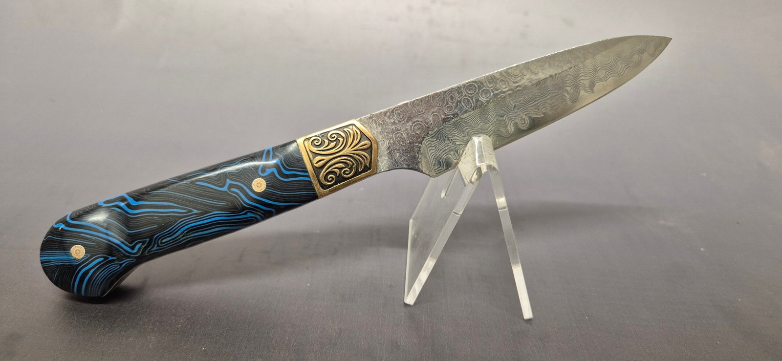 photograph showing the knife’s sculpted G10 handle, gold rivets